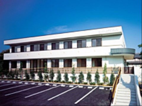 白色の施設である。広い駐車場が設けられており、奥には花壇がある。入り口までの道のりには手すりがついている。