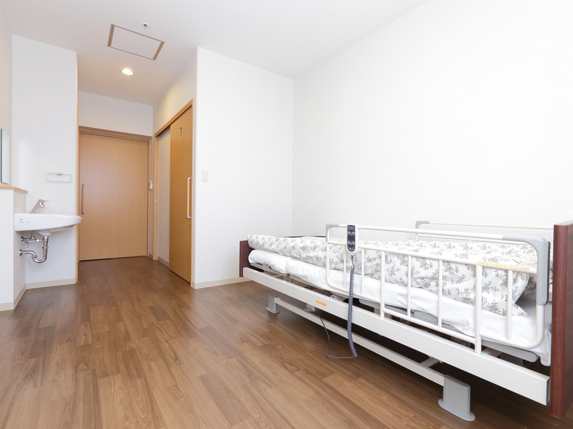居室の扉は引き戸である。右奥にトイレのドアがあり、左側に洗面台が設置されている。介護ベッドが置かれている。