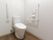 トイレの片側に、可動式の手すりが設置されている。サイドの壁には手すりや緊急呼び出しボタンが備わっている。