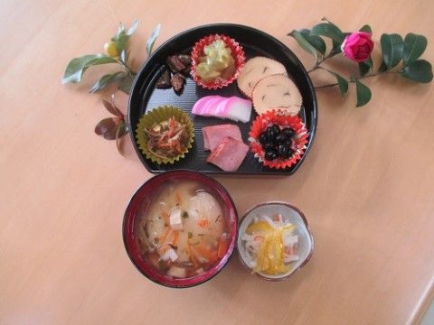 漆の皿に載せられた黒豆やかまぼこなどの料理や、味噌汁と酢の物