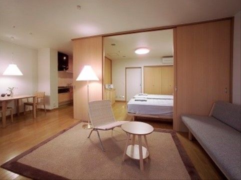 奥に扉で区切ることの出来る寝室があり、淡い色を基調とした家具の置かれたリビング