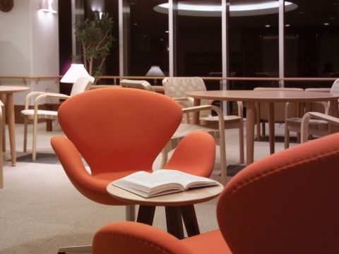 オレンジ色のゆったりした一人用の椅子が、小さな丸テーブルを挟んで２脚置いてある。奥には別のデザインの椅子が丸テーブルを囲んでいる。