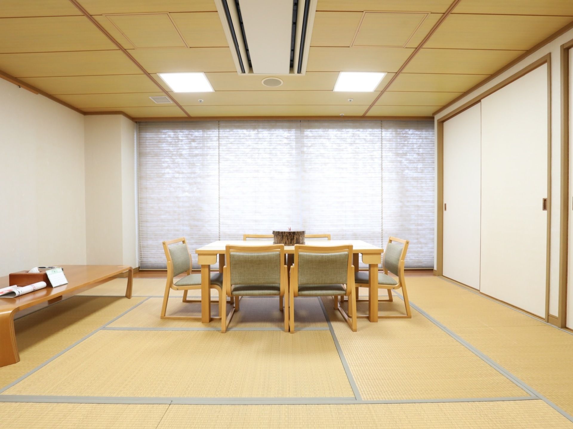 施設内には、畳の敷かれた広い和室の共有スペースが設けられている。中央には、椅子とテーブルが並べられている。