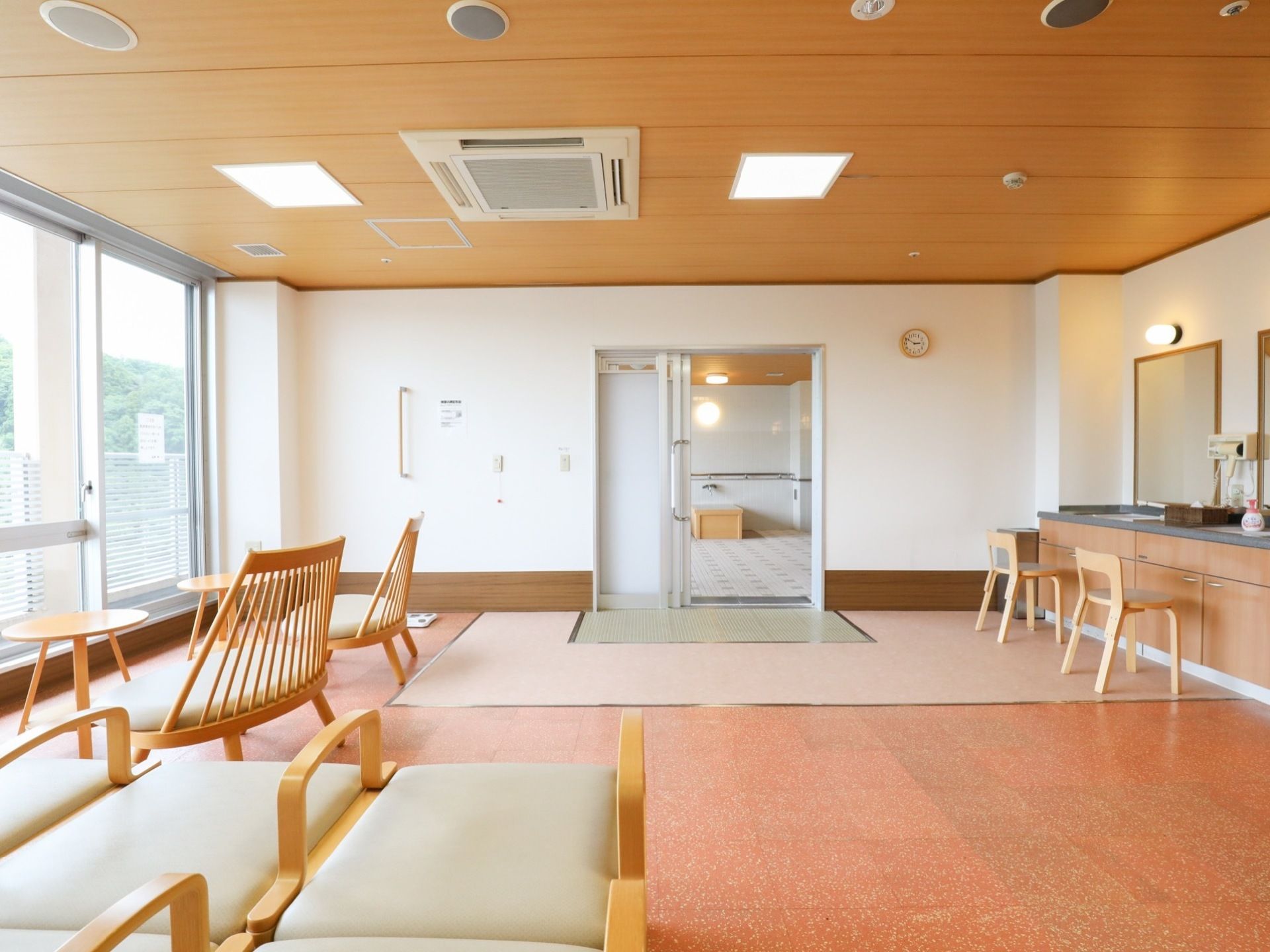 広い脱衣所には、椅子やベッドが並べられている。室内は赤色の床で、右側には鏡の設置された洗面スペースがある。