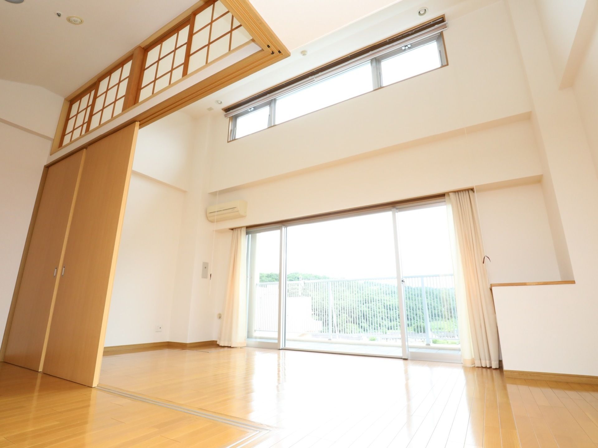 広々とした居室は天井が高く、全面がフローリングスペースになっている。奥には大きな窓が取りつけられており、白いカーテンが掛けられている。