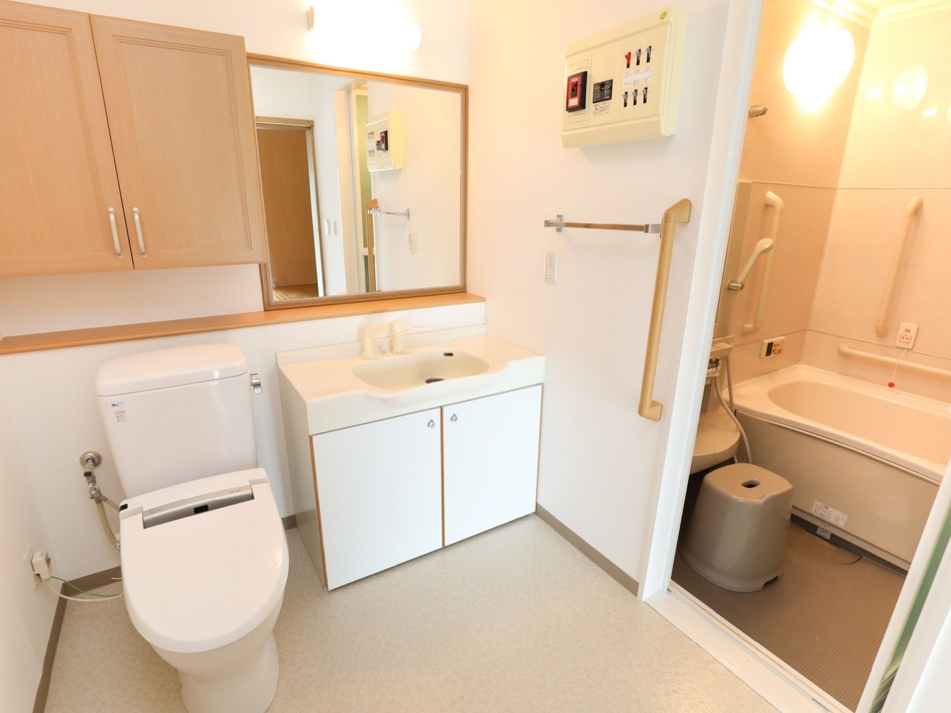 脱衣所には、洗面台とトイレが設置されている。壁には茶色い収納棚があり、隣りには四角い鏡が取りつけられている。