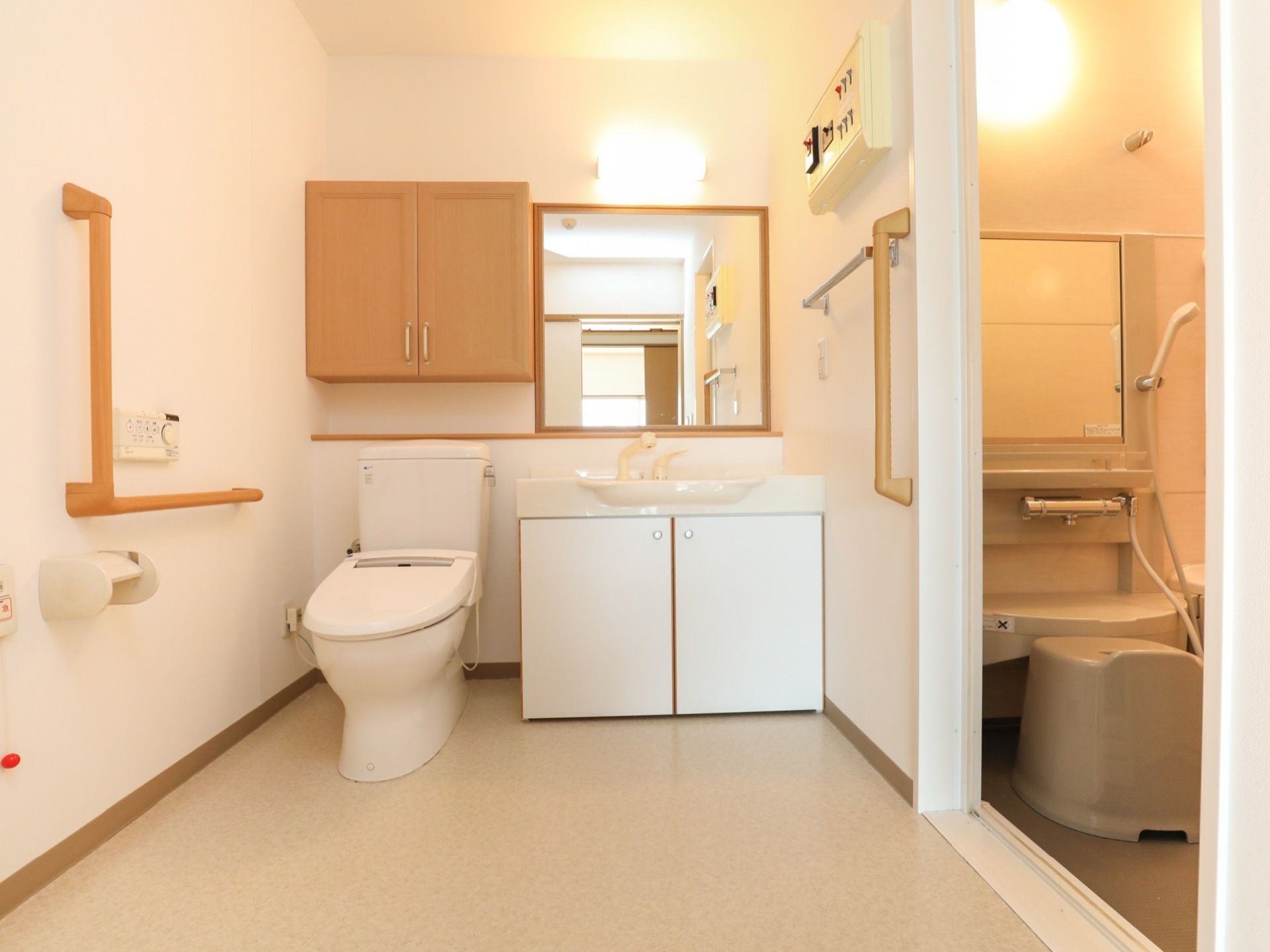 広々とした脱衣所には、トイレと洗面台が隣同士で設置されている。壁には、茶色い手すりが複数取りつけられている。
