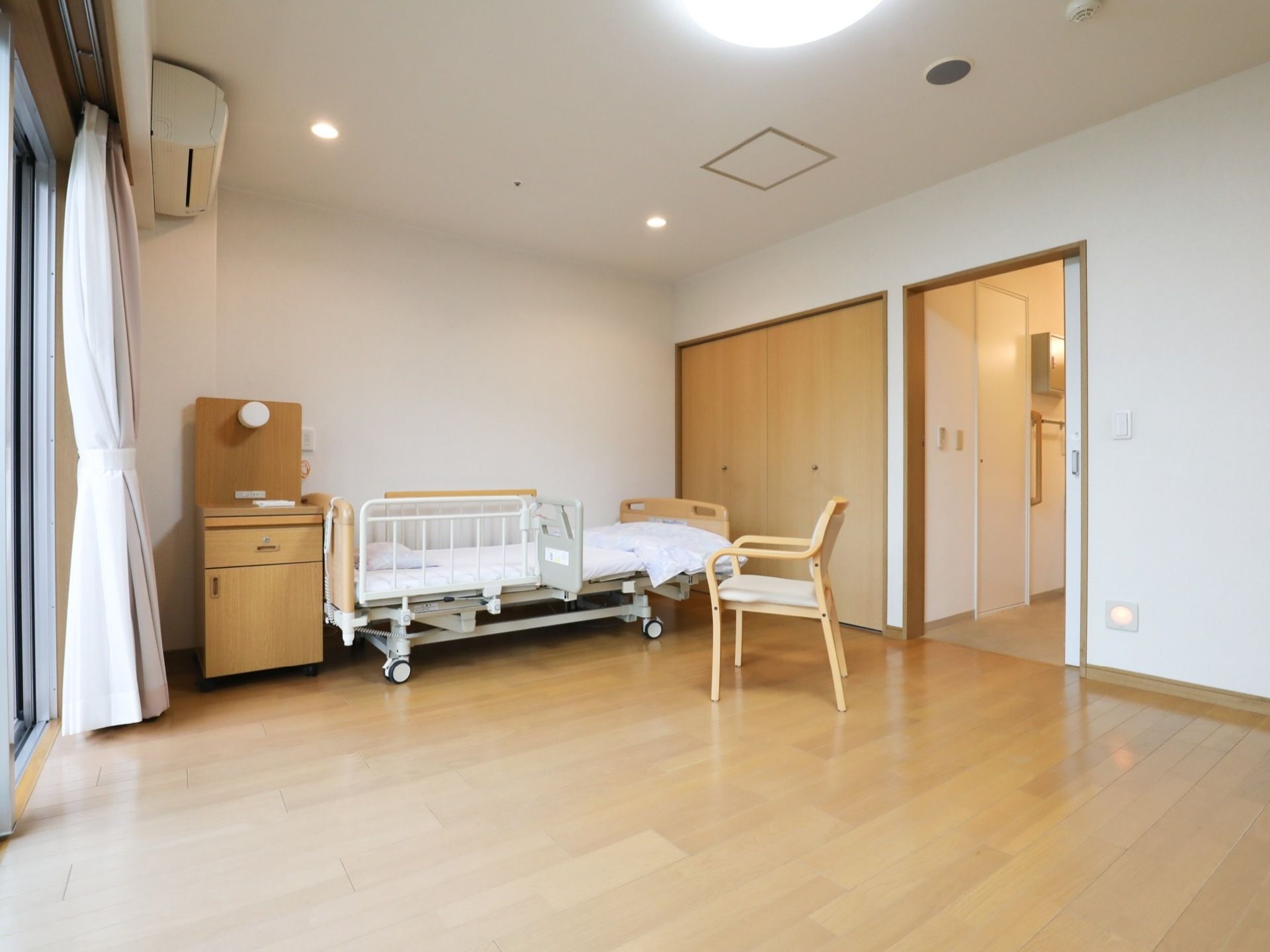 太陽の光が差し込む明るいお部屋である。ベッドには補助器具があり、高齢者の方でも安心してご利用いただける。