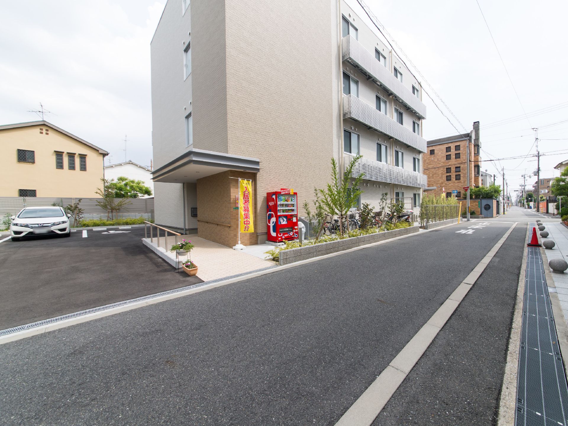 施設は4階建ての建物である。前面には道路が通っており、境にはフェンスと植え込みが設けられている。壁際に自動販売機がある。