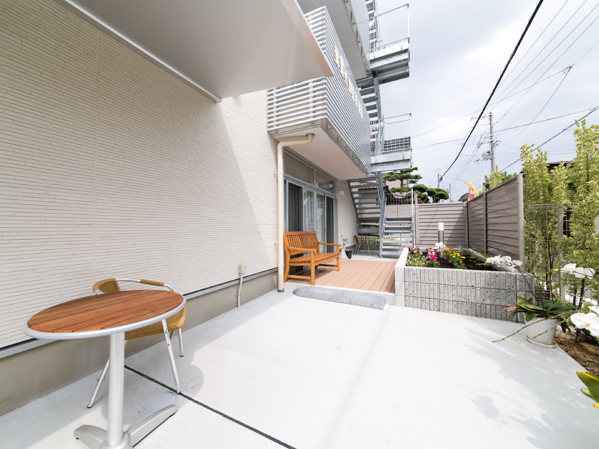 施設の建物には窓の外にデッキが設けられており、木製のベンチが1つ置かれている。前面にはブロックで囲われた花壇がある。