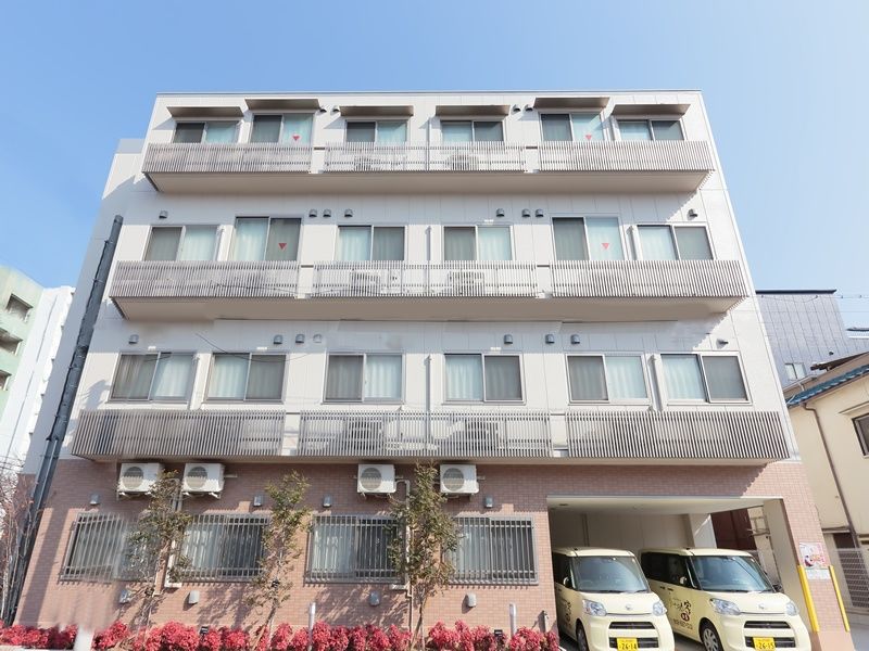 施設は道路の交差点部分に建っている。4階建ての建物で、外壁はブラウン系とアイボリーに色分けされている。駐車場がある。