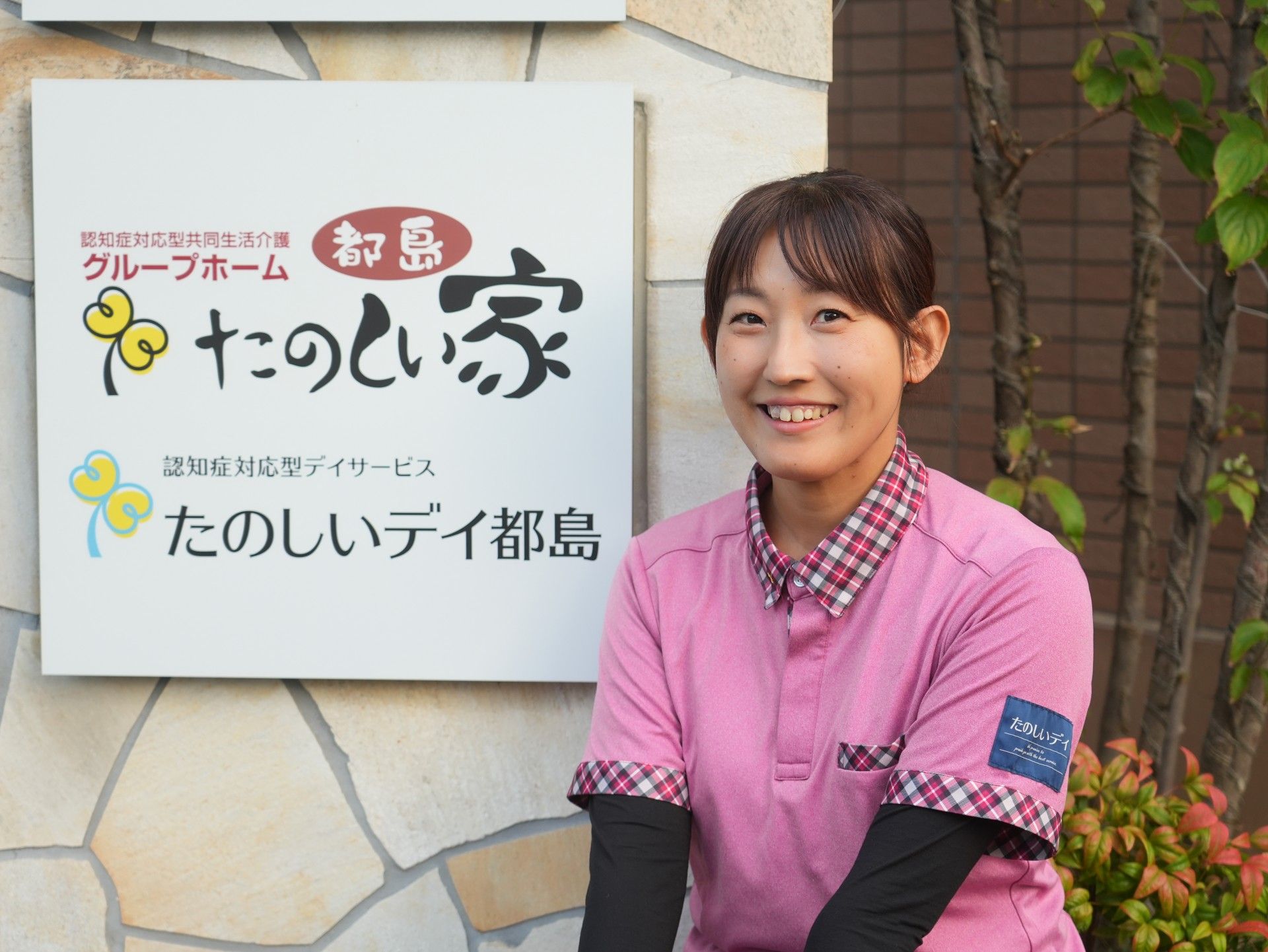 樹木とツツジが周りに植えられた4階建ての建物の一角