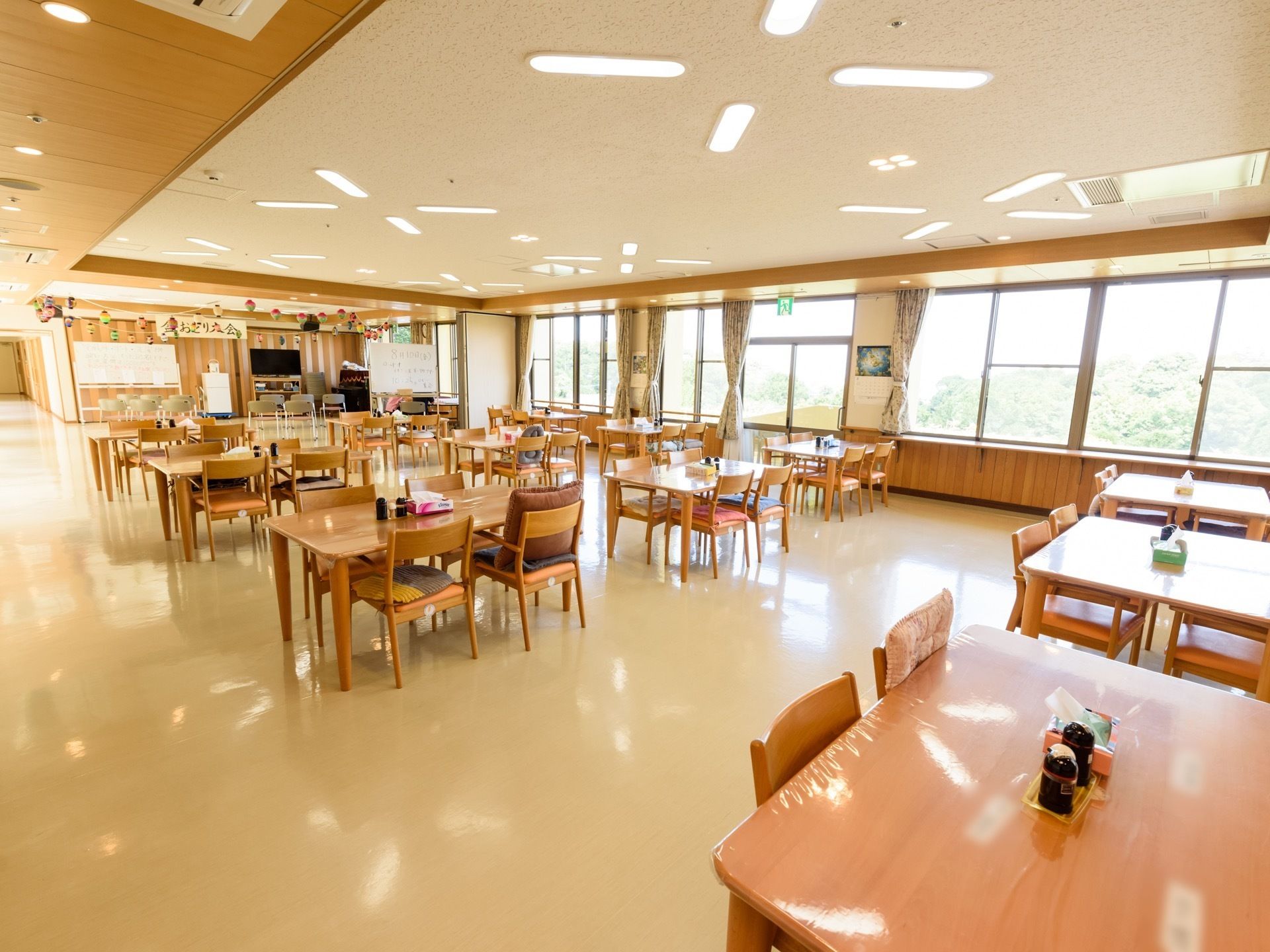 白い床と木目のテーブルや壁、天井、壁一面の窓がとても明るく開放的な食堂である。通路の間隔は広く取られている。