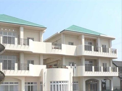 ベランダのある白い壁面にミントグリーンの屋根の3階建ての建物