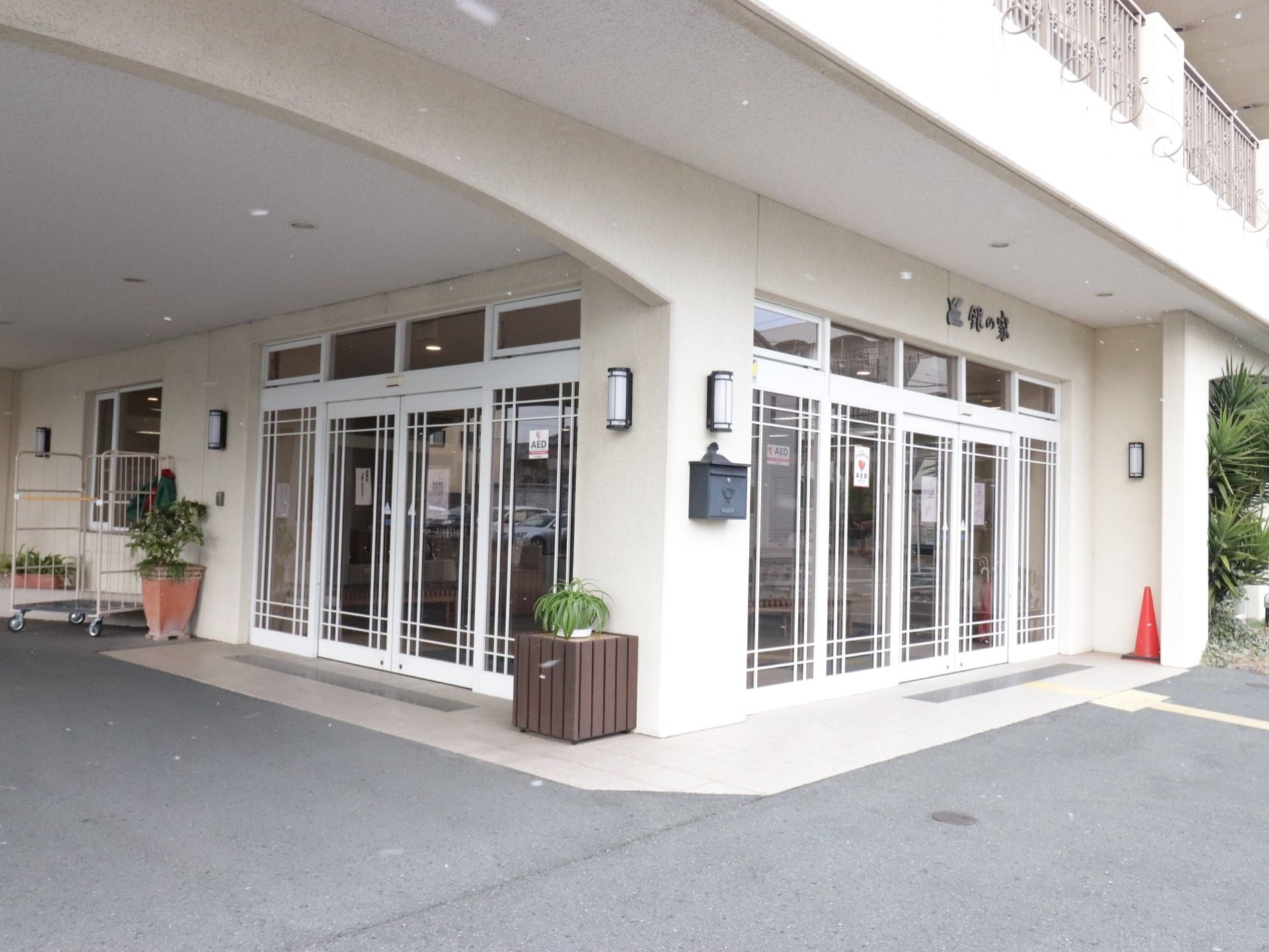 白基調の広い外玄関である。ポストや観葉植物、AED表示もある。2方向から入ることができるようになっている。