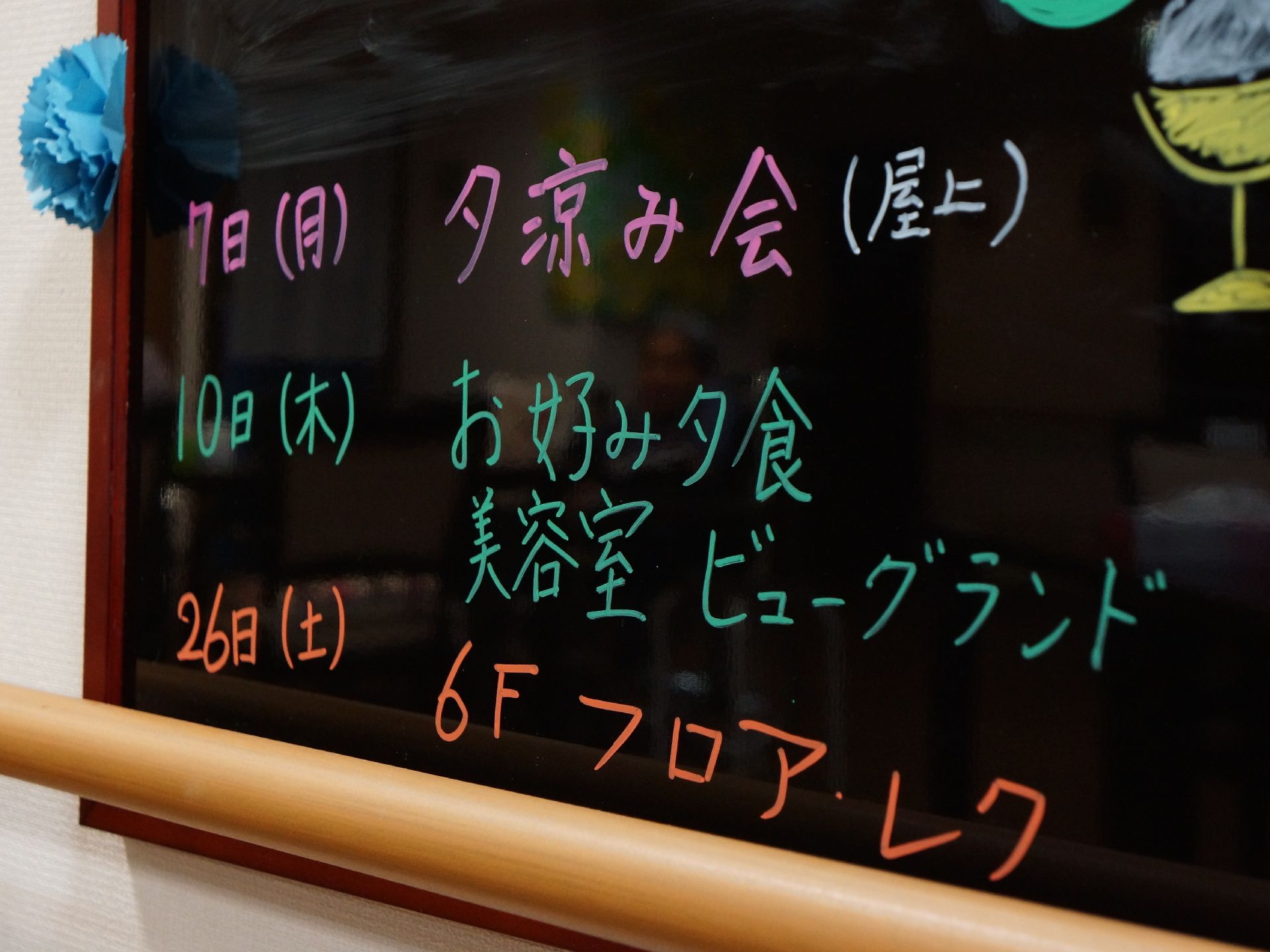 白壁に茶系の枠の黒いボードが設置。ボードには、予定が掛かれ、カラフルな文字で明るく、一部には絵も描かれている。