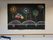 白壁には、額縁の絵画が飾られ、その横に花火をモチーフの手作り作品が貼られている。その下には手すりが設置してある。