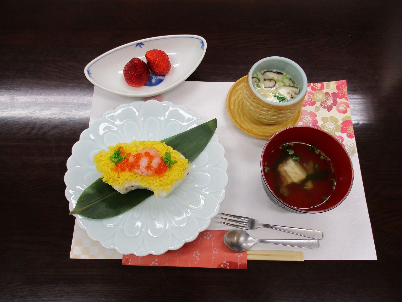 黒色のトレー上の手前にご飯と汁物、上にはメインのおかずが置かれ、2つの小鉢とお茶が添えられた食事メニュー。