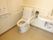 洗面台が備え付けられた個室トイレである。壁にＬ字型の手すりや操作パネル、ペーパーホルダーが設置されている。