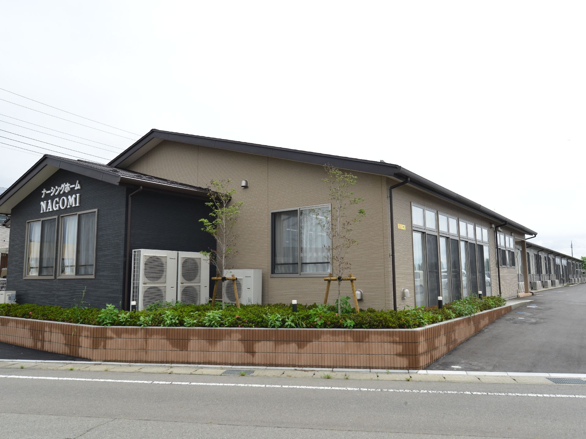 道路側から見た施設の画像。広々とした敷地に1階建ての縦長の施設と、ゆとりのあるスペースで駐車場がある。