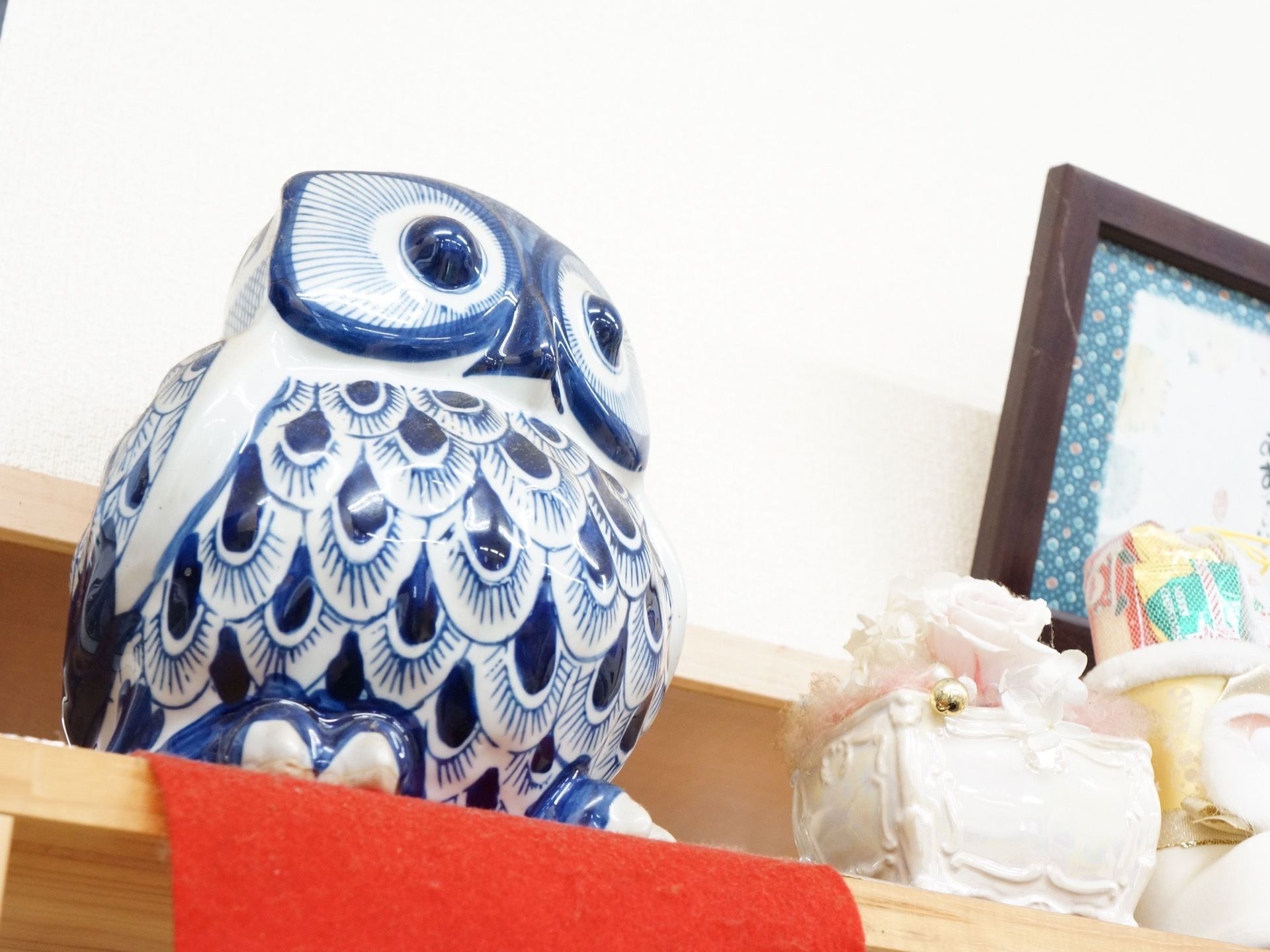 棚の上に、陶器でできた青いフクロウの置物が置かれている。隣には陶器に入った造花、お菓子の入った長靴がある。