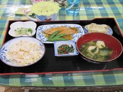 魚の照り焼きや、おひたしなどさまざまなおかずが用意されている。ご飯は白米ではなく炊き込みご飯が用意されている。
