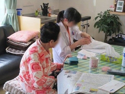丸テーブルの席に付き、新聞を広げて白衣の女性と話をする高齢者