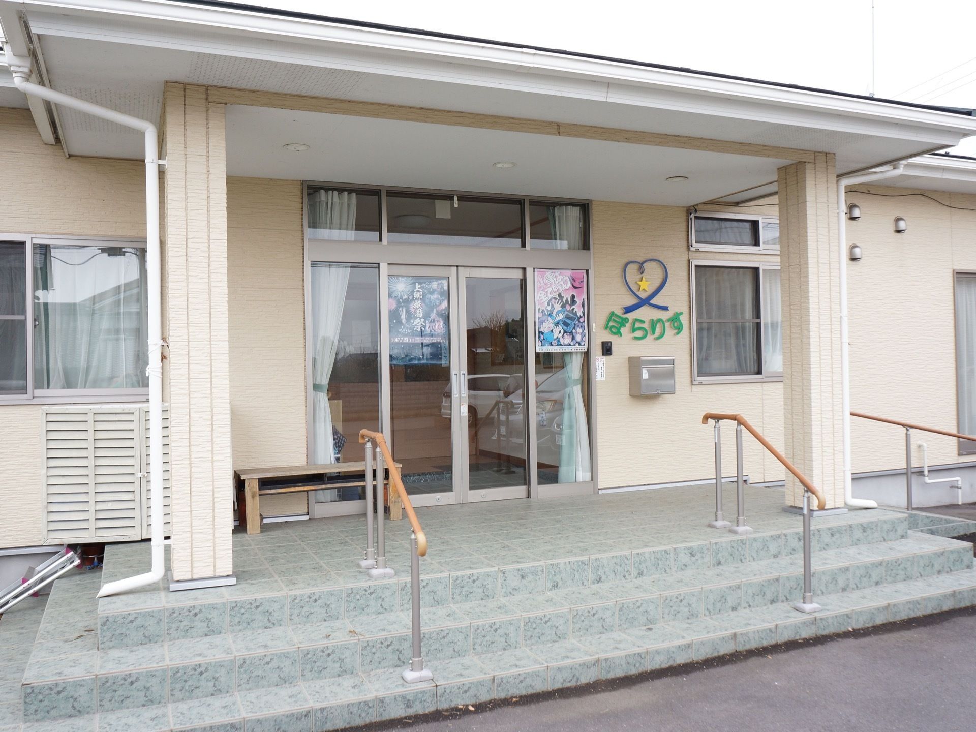 手すりのついた階段を上った先にある、地域のイベントのポスターが貼られた玄関