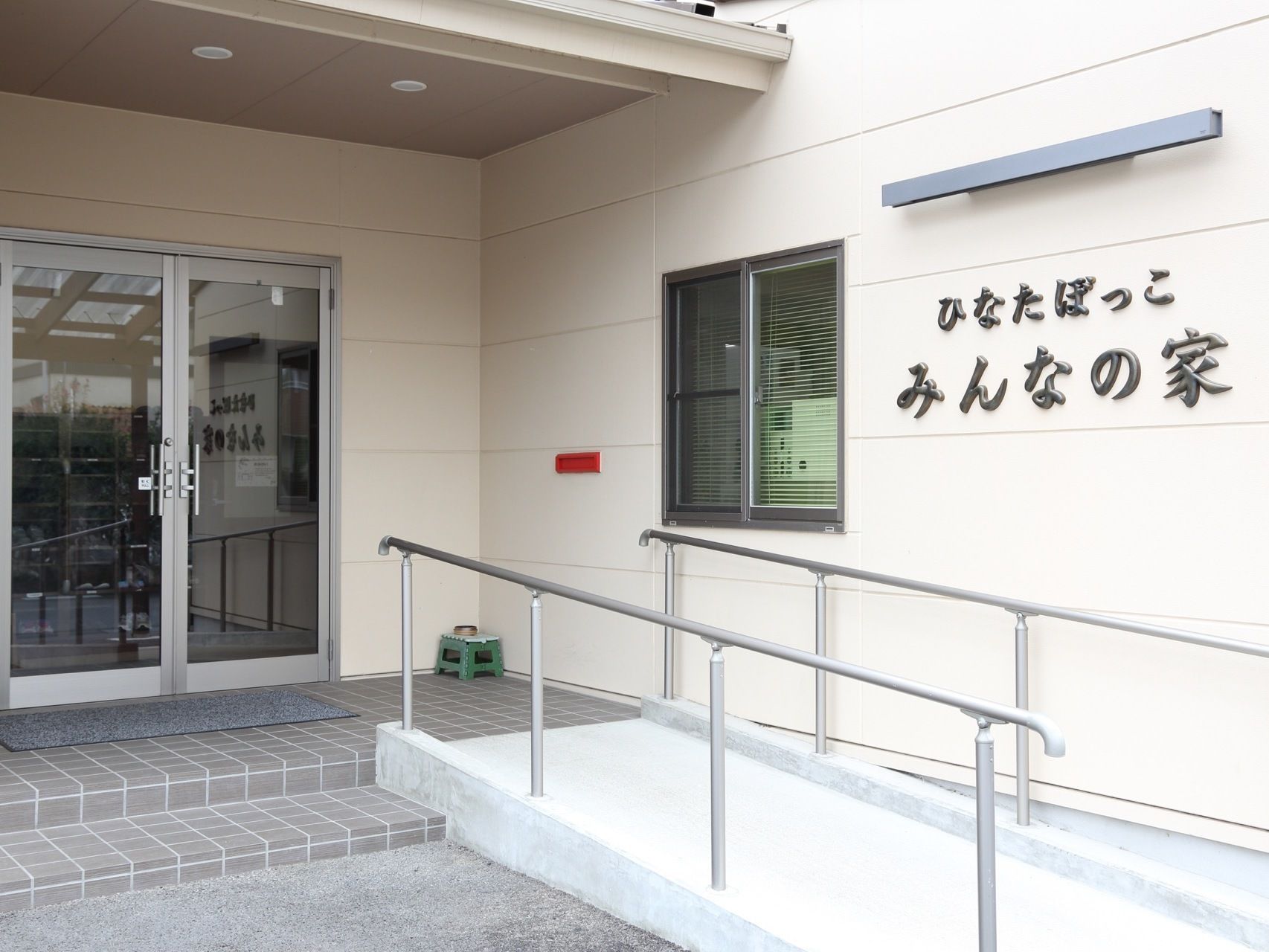施設は、白系の色をした建物である。玄関に向かって右手にはスロープが設置されている。スロープそばの壁にはダークグレーで施設名が表示されている。