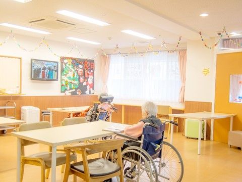 クリスマス飾りのつけられた共有スペースで車椅子に座り、テーブルにつく高齢者