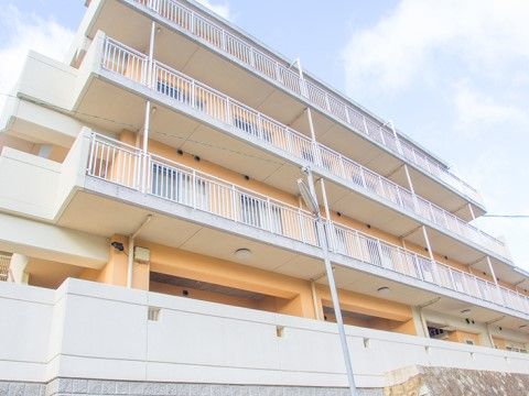 パウダーオレンジと白い壁が優しい印象を与える、３階建ての真新しい建物。居室部分にはベランダが付いている。