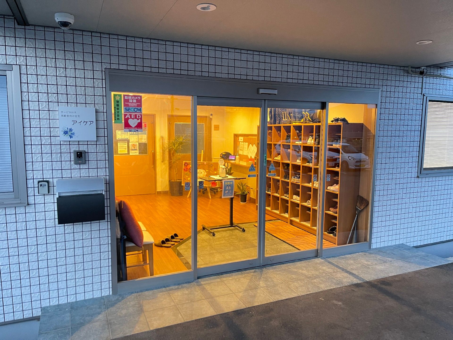 入り口は自動扉になっている。外壁には施設名が記された看板が設置されており、インターホンとポストが用意されている。