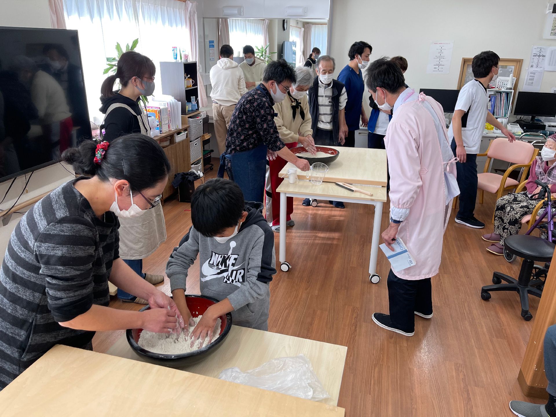 共有スペースでは、スタッフと入居者様が楽しそうに掲示物を作成している。テーブルの上には折り紙などが置かれている。