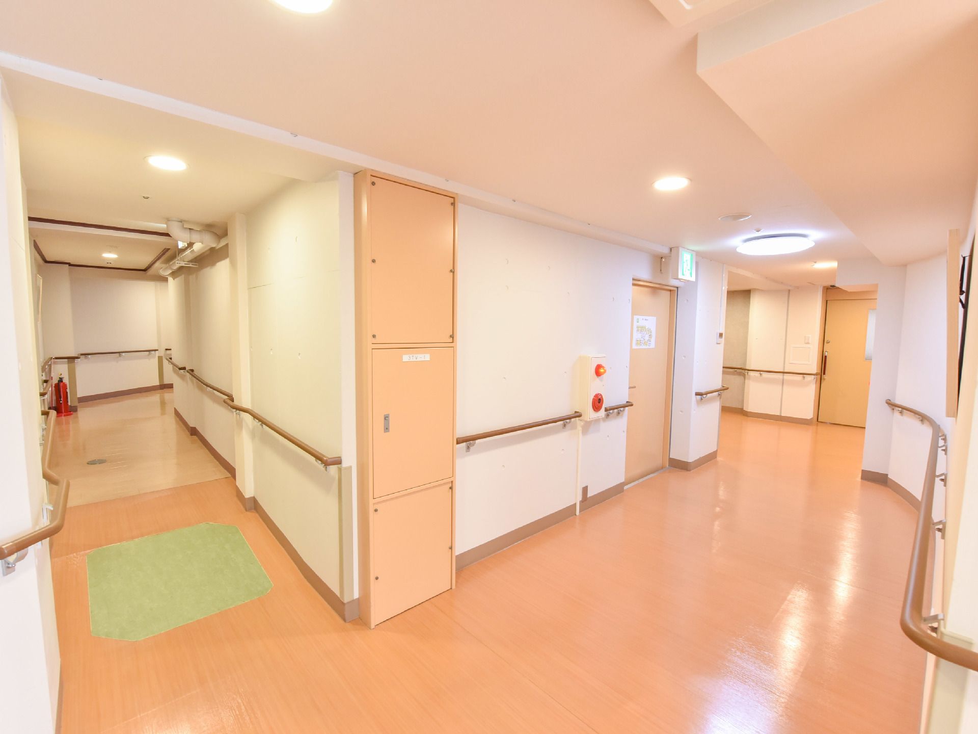 左に続く廊下は少しスロープになっていて、角に消火器が置かれている。右の廊下にはドアがある。壁が少しカーブしている。