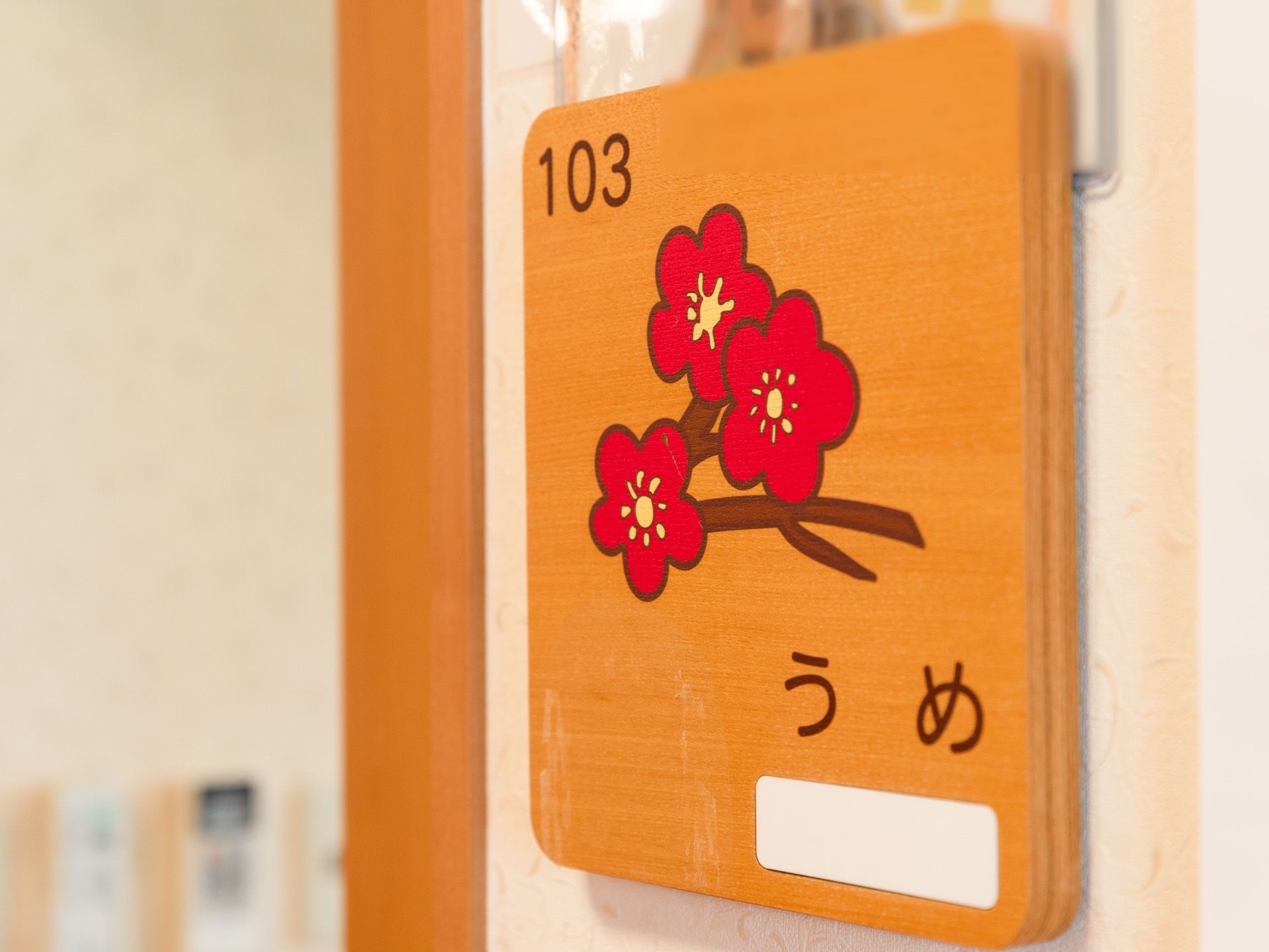 居室の扉横の壁には、木製の表札が設置されている。部屋番号と花の絵が描かれており、入居者様の氏名を記入するスペースがある。