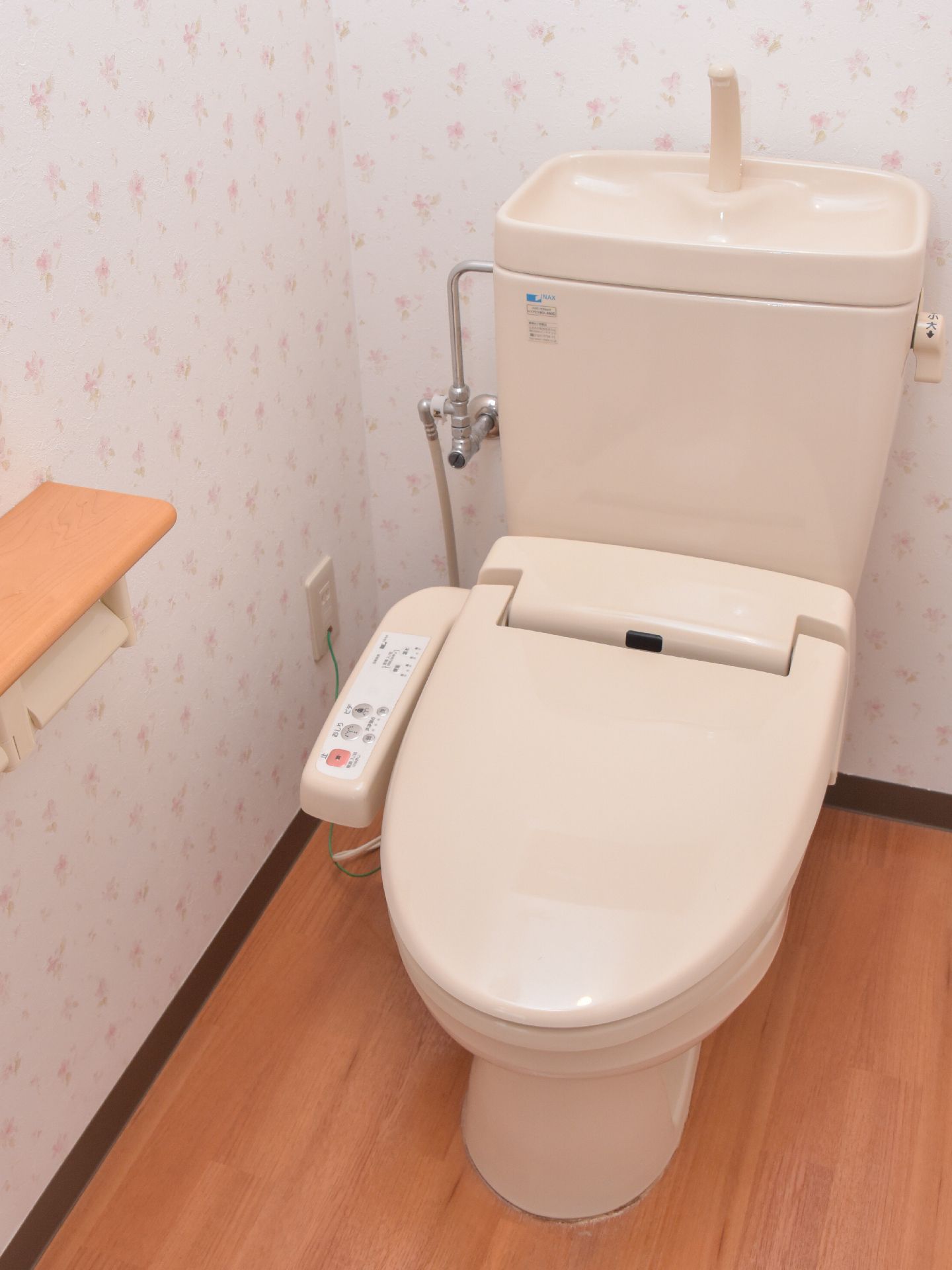 ブラウンの床と花柄の壁紙が明るい雰囲気のトイレ。ピンク系のトイレが設置してあり全体的な統一感もある。