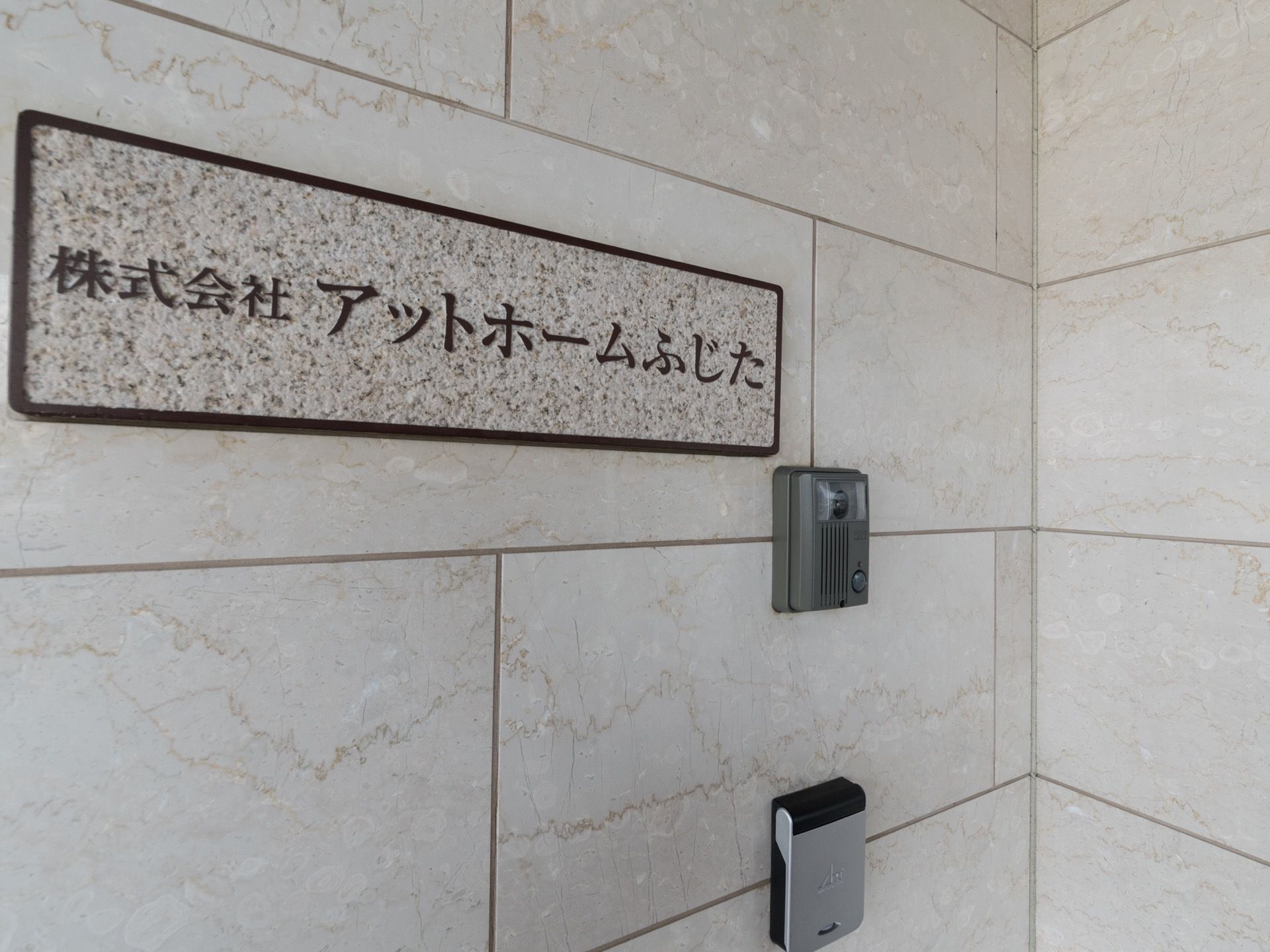 玄関に施設名の看板が掲げられている。モニター付きインターホンが設置されており、セキュリティ対策が行われている。