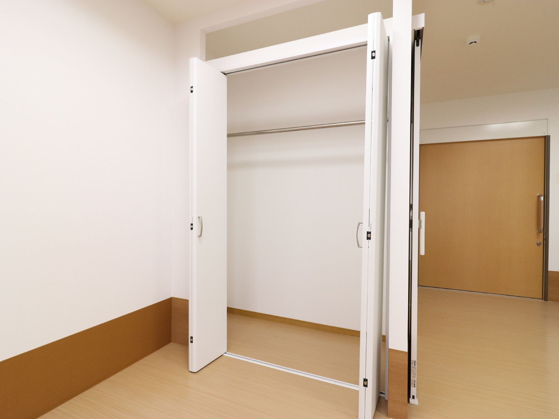 白い扉のクローゼットにはハンガーラックが備えられている。キッチンの横には窓と食器棚がある。また、キッチンの上下にも収納スペースがある。