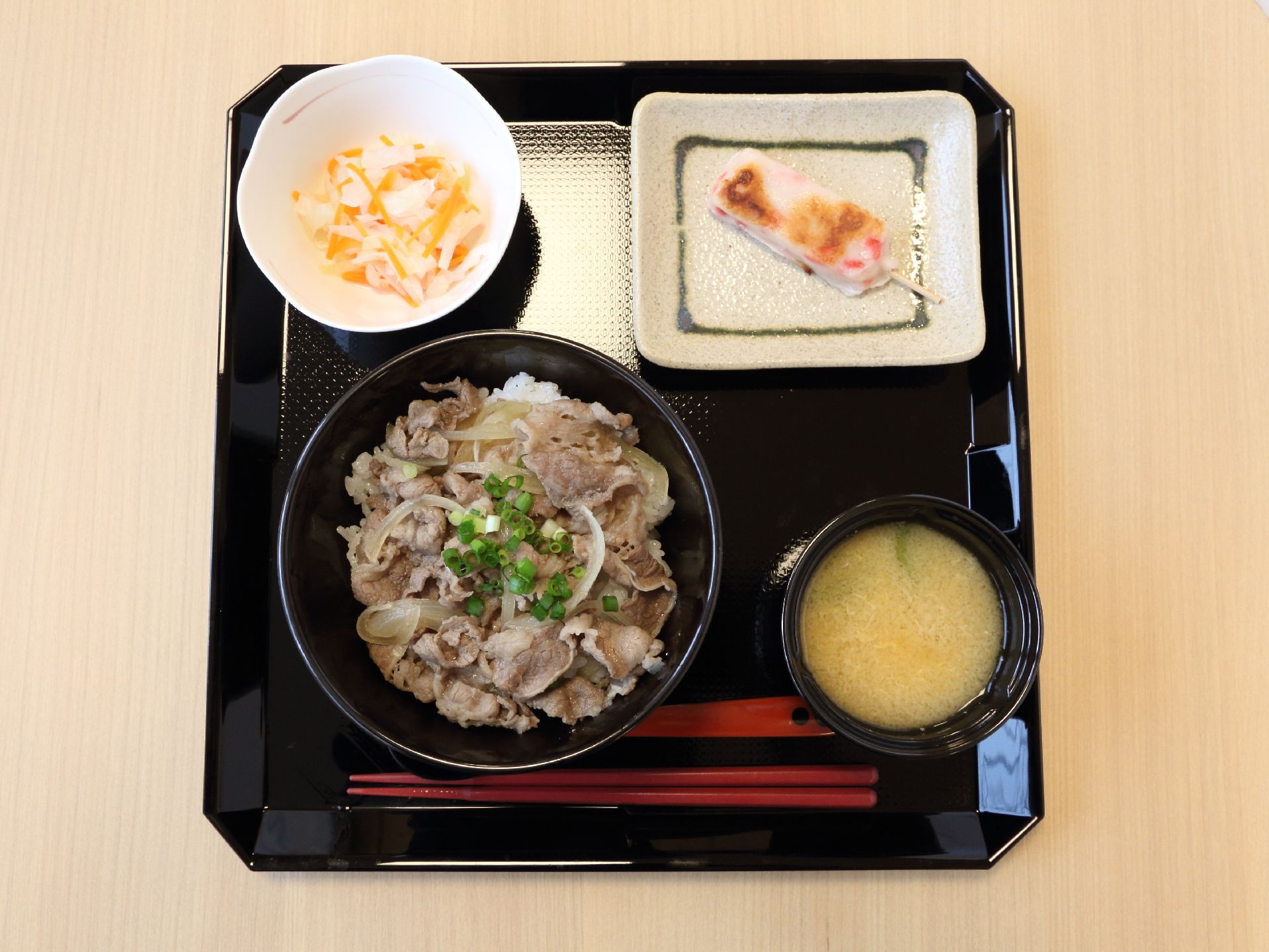 食事が黒いトレーに置かれている。牛丼や野菜の和え物、みそ汁など、栄養バランスが考えられた食事を摂ることがでできる。