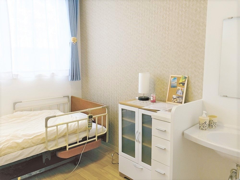居室内には洗面所が設置され、介護用ベッドや収納家具が置かれている。窓にはカーテンが付けられ日当たり良好。