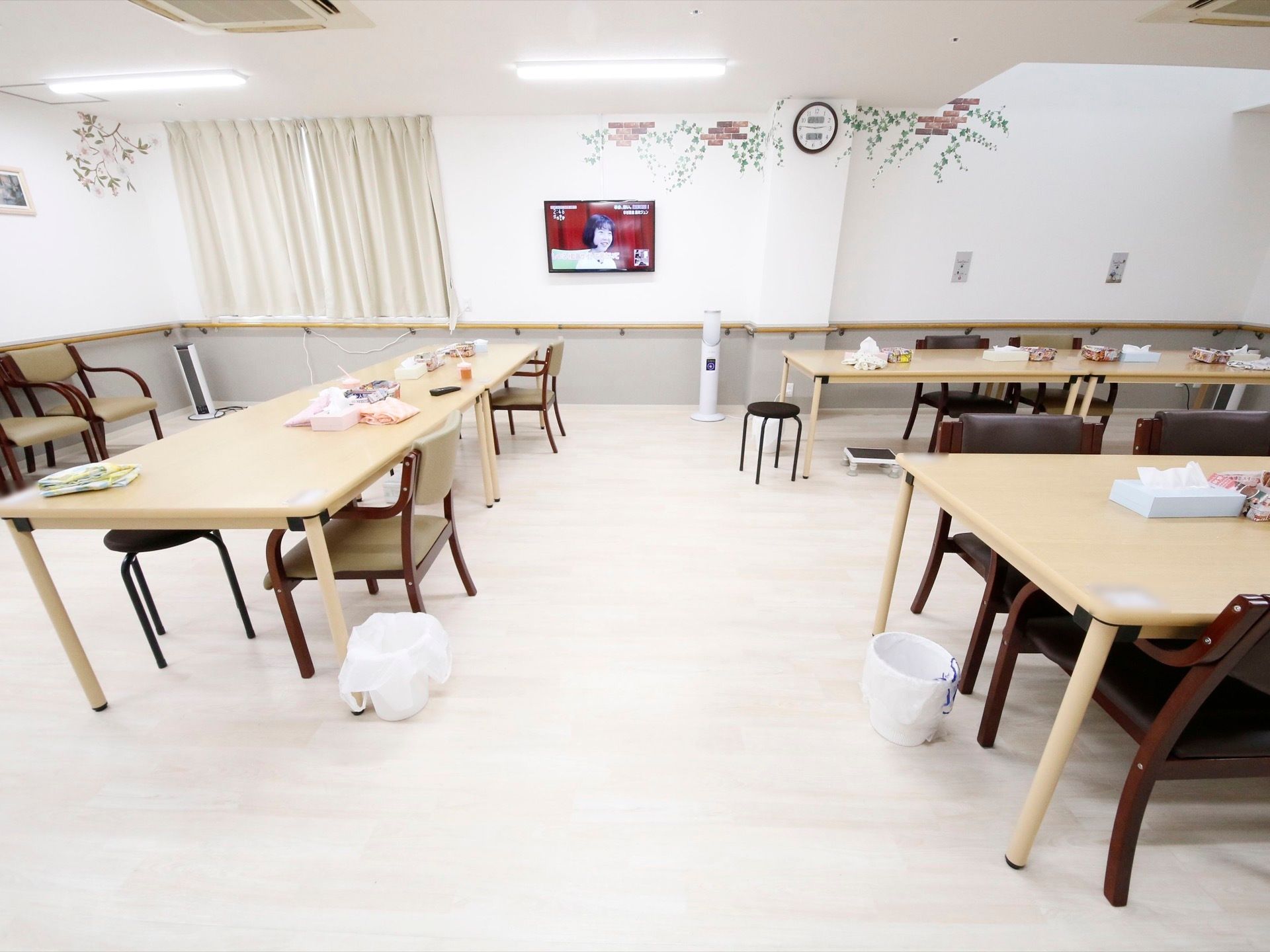 白を基調とした広い空間に大きなテーブルが３台あり、その下にゴミ箱がある。壁にテレビが取り付けてある。