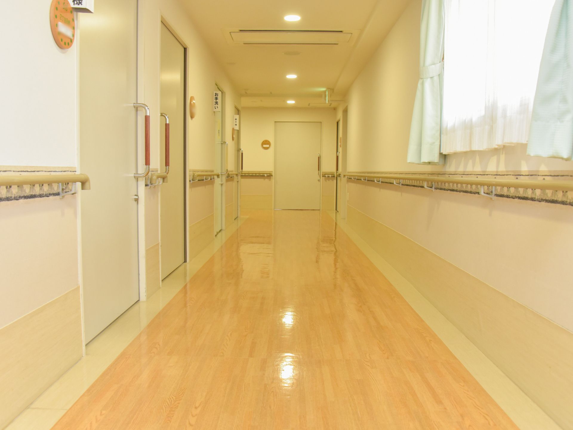 廊下には窓があり、明るい雰囲気。居室には、名前が表示されている。壁一面に手すりがあり、安全に移動が可能。