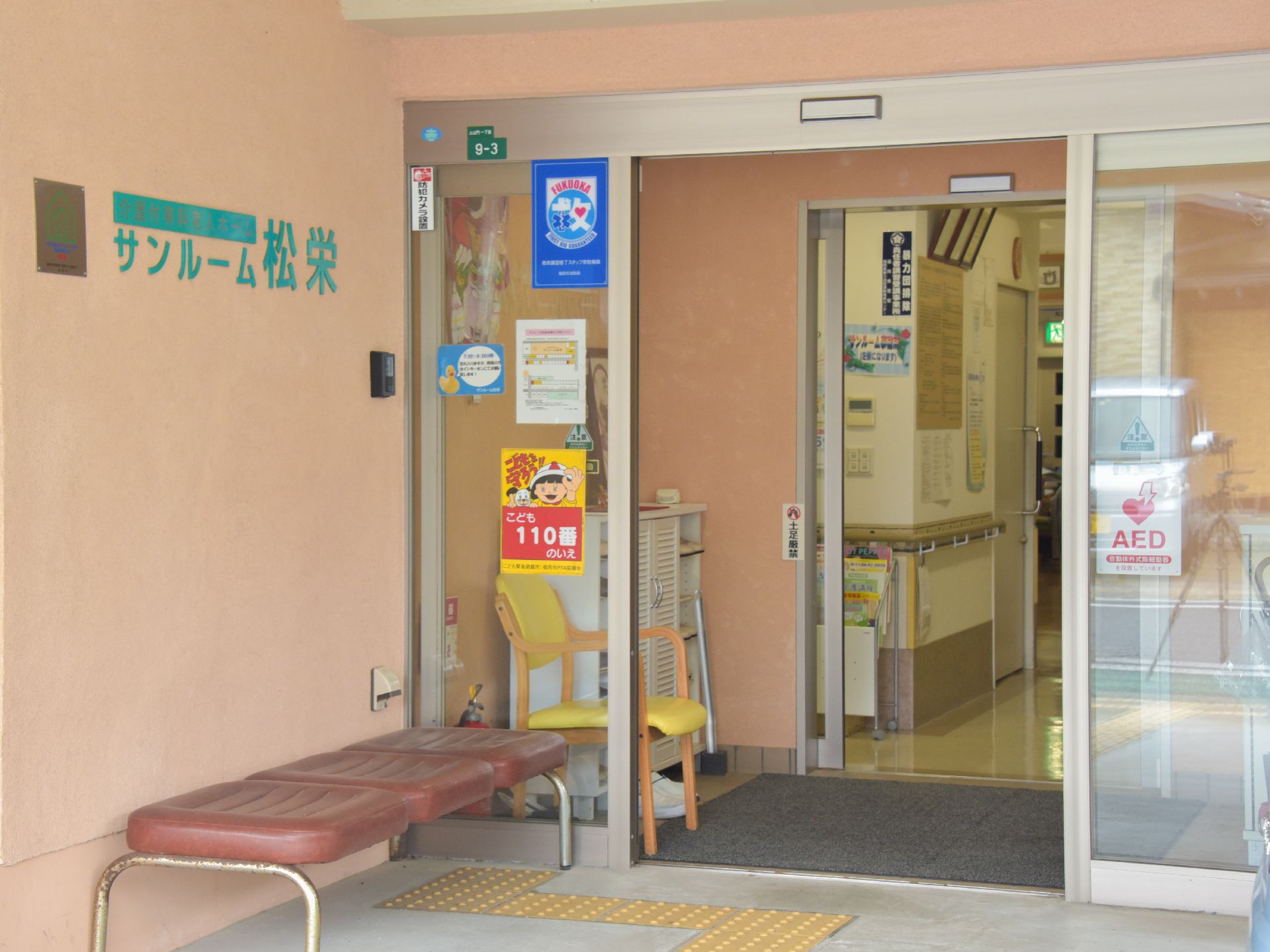 施設の入口。内外に、椅子が置かれている。防犯カメラも設置されている。入居時や通院時には、送迎も行われる。