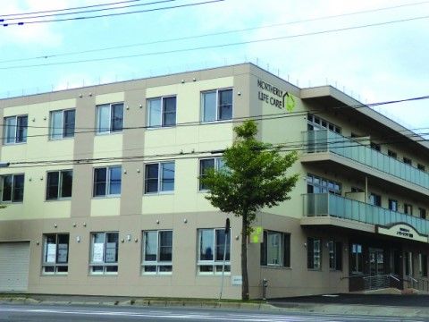 大きな木の側に立つ長いベランダのある3階建ての建物