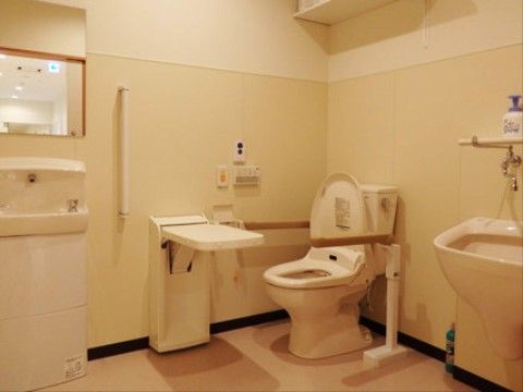 洋式便器が設置されていて、車椅子も入れるよう、通路が広い。壁面に手すり、手洗い用洗面台が設置されている。