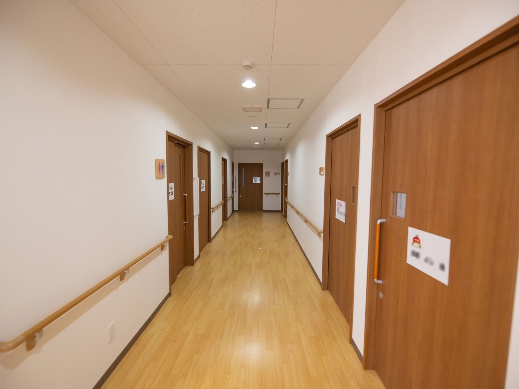 真っ直ぐな見通しの良い廊下である。両サイドに居室やトイレのドアが並んでおり、壁に沿って手すりが取りつけられている。