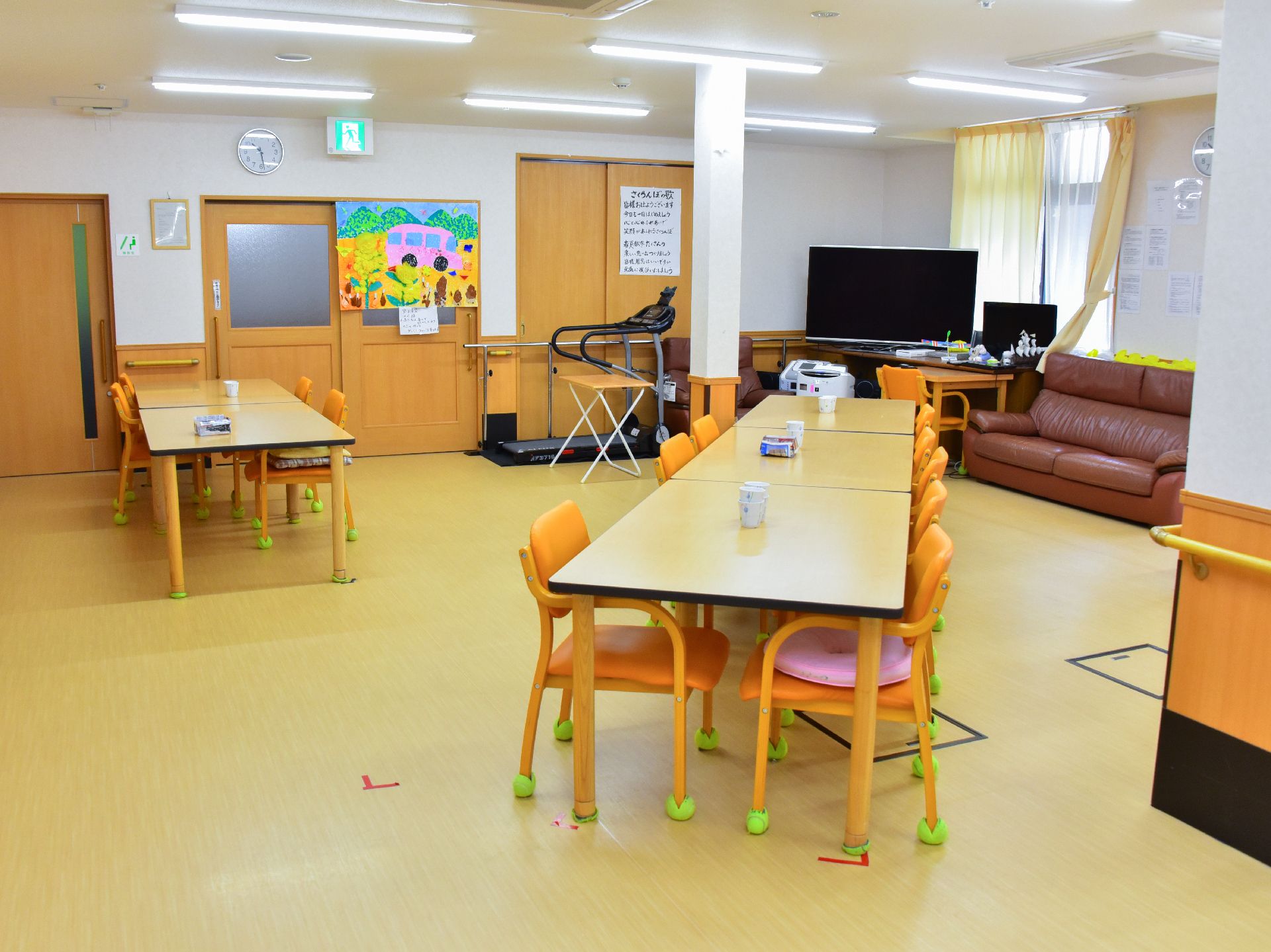 沢山のテーブルと椅子が置かれ、ランニングマシンやテレビなどの設備がある共有スペース