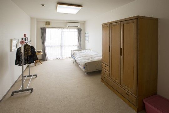 正面に大きな掃き出し窓があり、左手には丸テーブルとハンガーラックがある。向かの壁にはガード付きのベッドが置かれている。
