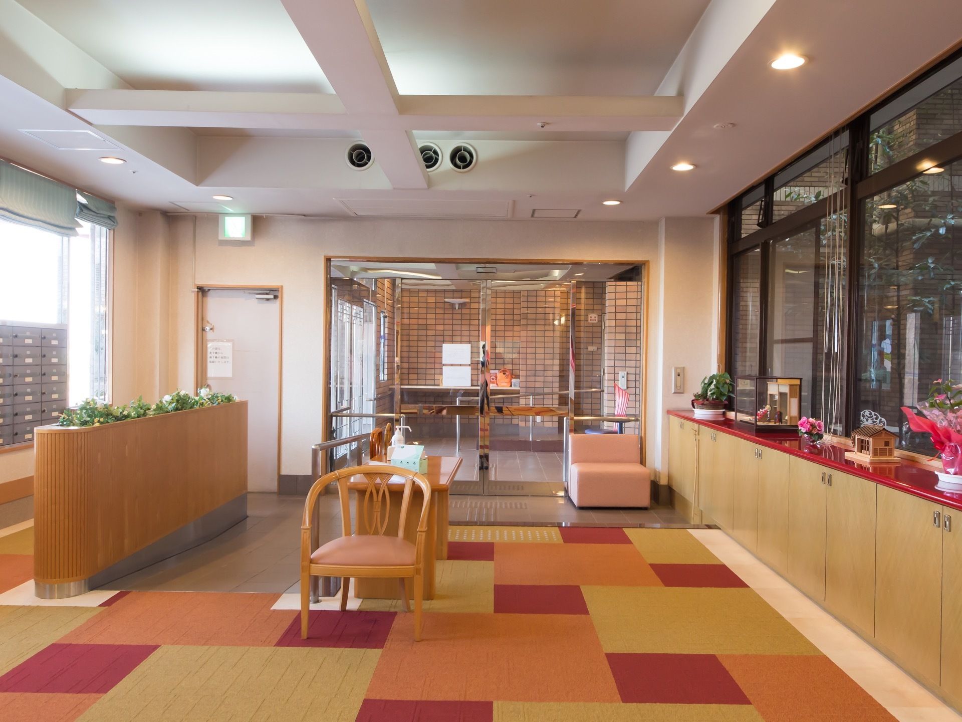 手すりの付いスロープが備わっている。消毒液が置かれている。間口の広い自動扉になっている。手荷置き場として椅子が用意されている。
