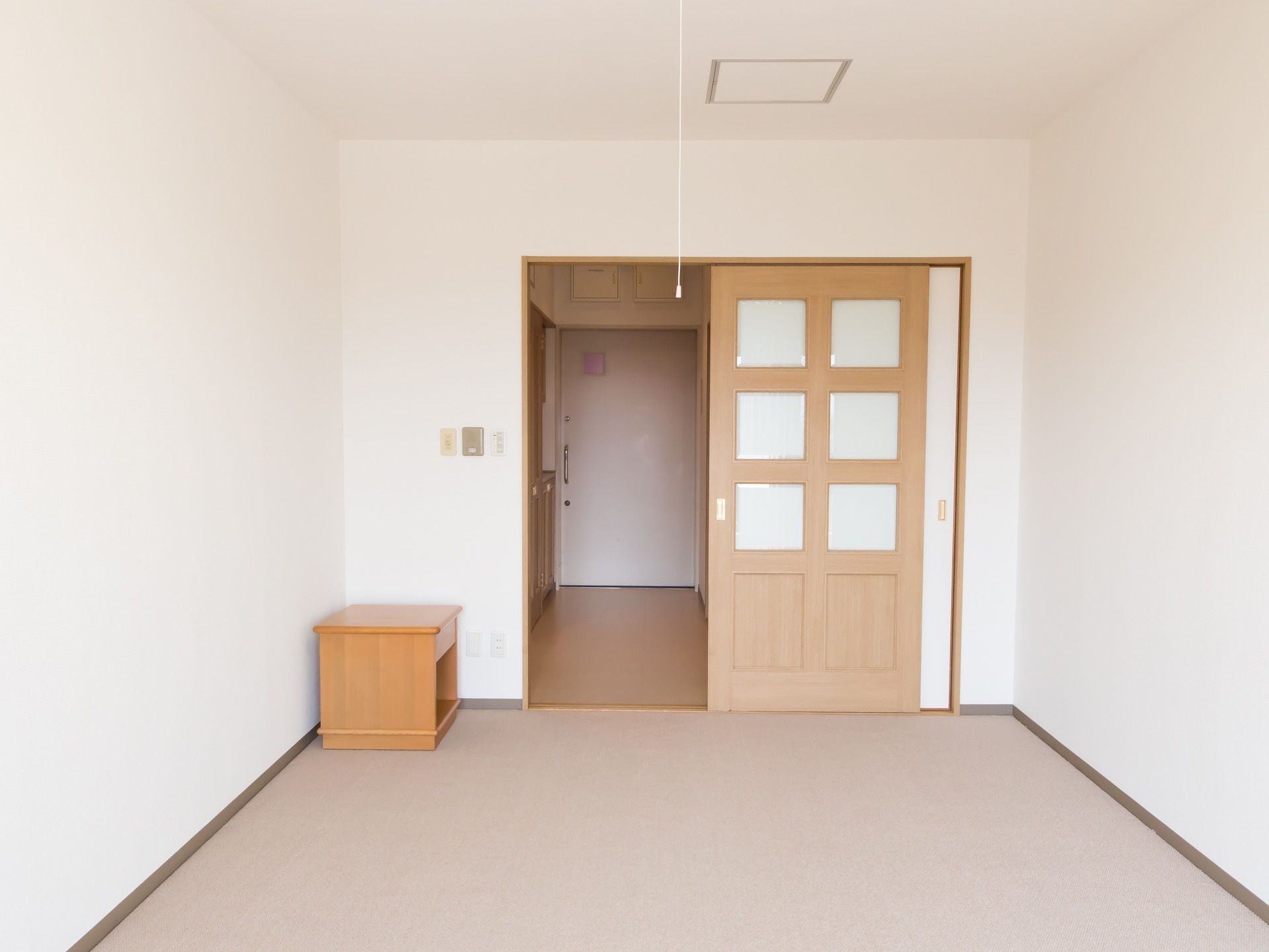 白で統一されており、開放的な空間である。段差のないフローリングである。小さなチェストが置かれている。